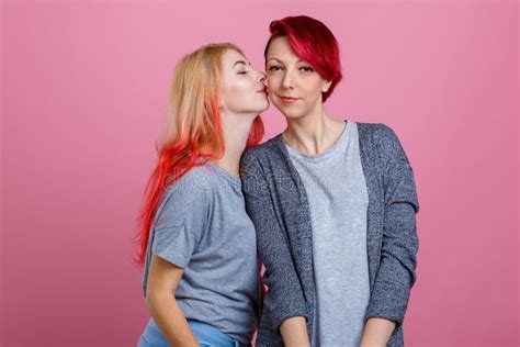 Dos Muchachas Lesbianas Una Besan Otra En La Mejilla En Un Fondo Rosado Foto De Archivo
