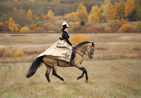 Фото Наездница в черной шляпе черной куртке и в бежевой юбке скачет на лошади по полю вдали