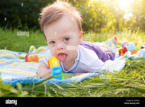 Portrait Of Cute Baby Boy With Down Syndrome Lying On Blanket In Summer