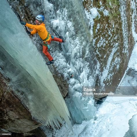 Aerial Perspective Of Ice Climber Ascending Frozen Waterfall In Canyon