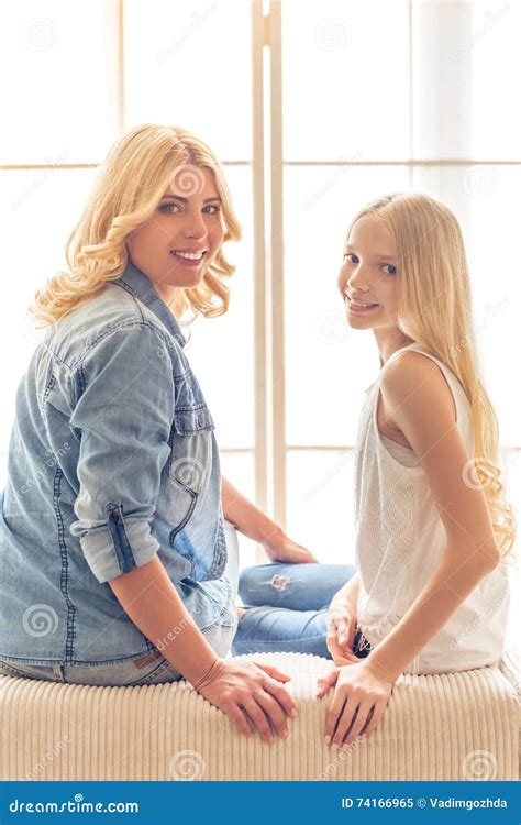 Beautiful Smiling Blond Mother And Daughter Are Sitting On The Couch In