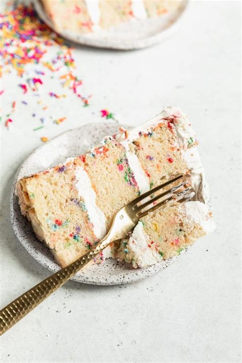 A Slice Of Cake With White Frosting And Sprinkles On A Plate