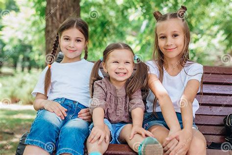 Drei Süße Kleine Mädchen Lächeln Und Sitzen Im Sommerpark Auf Der Holzbank Stockfoto Bild Von