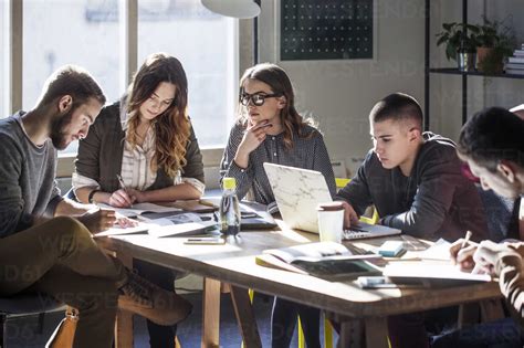 College Students Studying While Sitting At Table By Window In Classroom