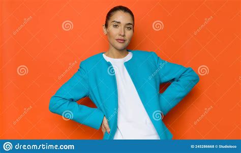 Young Woman Poses In An Unbuttoned Blue Jacket On Orange Background