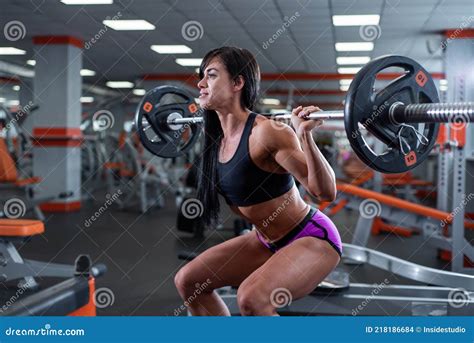 A Strong Muscular Dark Haired Girl Performs Squats With A Light