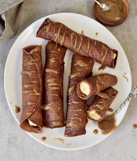 A White Plate Topped With Chocolate Covered Crepes Next To A Jar Of