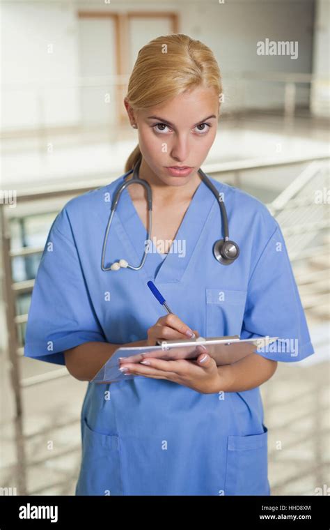 Serious Nurse Writing On A Clipboard In Hospital Corridor Stock Photo