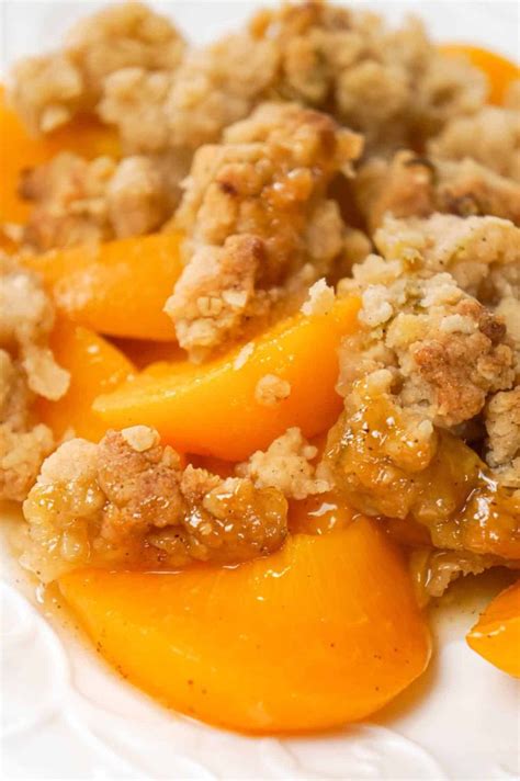 A White Plate Topped With Sliced Peaches And Crumbled Topping On Top Of It