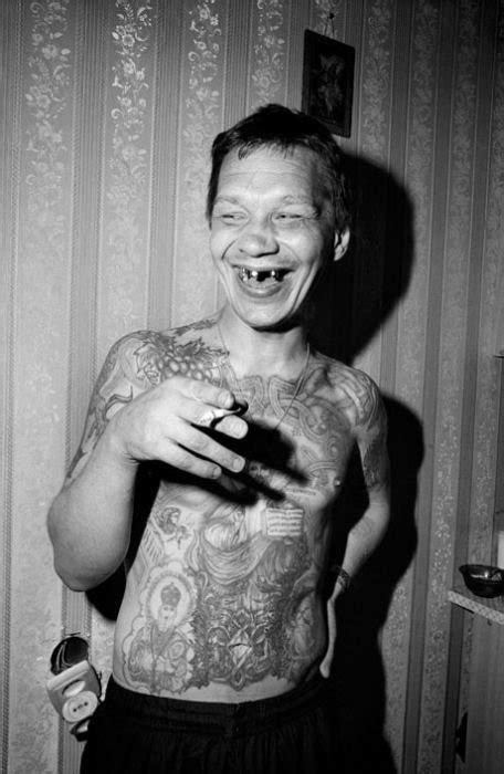 A Man With Tattoos On His Chest Holding A Cell Phone And Smiling At The