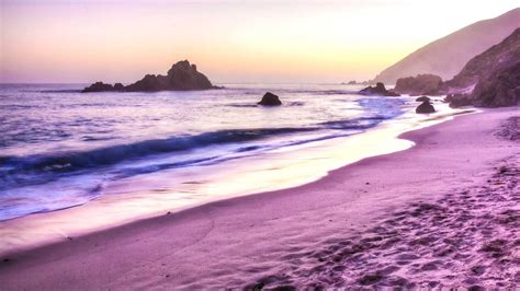 The Beach Is Covered In Purple Sand As The Sun Sets Over The Ocean And