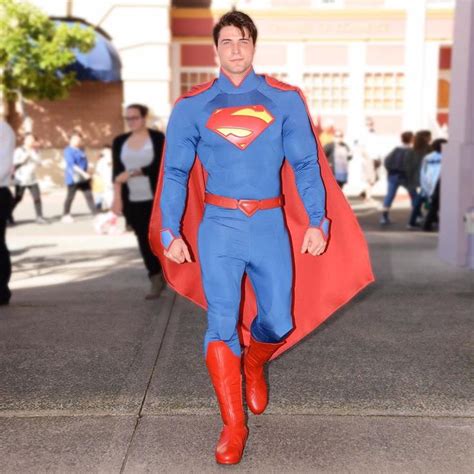 A Man In A Superman Costume Is Walking Down The Street With His Hands