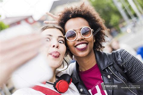 Two Women Sticking Out Tongues While Taking Selfie With Smartphone