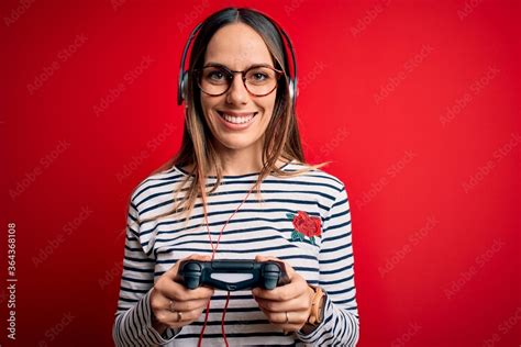 Young Blonde Gamer Woman Using Gamepad Playing Video Games Over Red