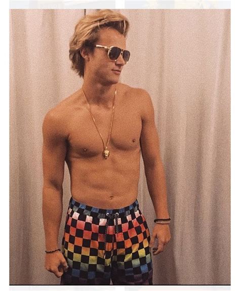 A Man With No Shirt Wearing Colorful Checkered Swim Trunks And Gold