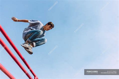 From Below Of Brave Male Jumping Over Metal Fence In Street And Showing