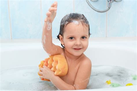 Cheerful positive adorable small child taking bath and washing herself ...