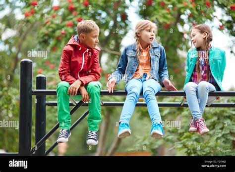 Happy Kids Talking While Sitting On Recreational Facilities Stock Photo