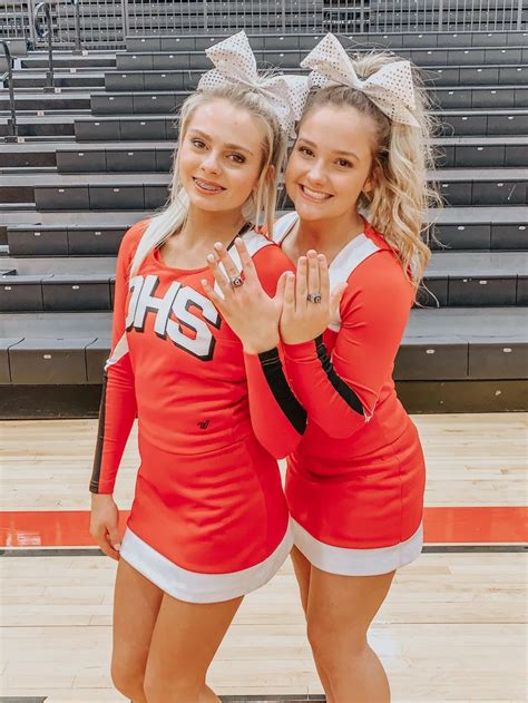 Two Cheerleaders Posing For The Camera In Front Of Bleachers