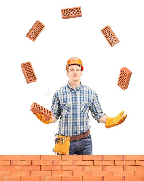 Construction Worker Juggling With Bricks Behind A Brick Wall Stock