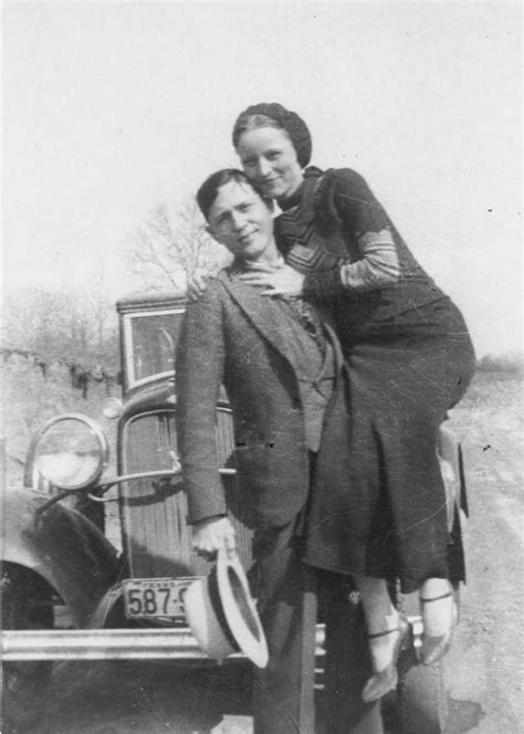 an old black and white photo of two people standing next to each other in front of a car