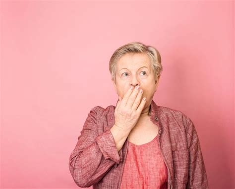 premium photo scared and shocked senior woman close mouth with her hand over pink background