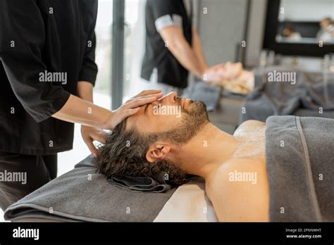 Two Masseurs Doing Facial Massage To A Couple At Spa Salon Wellness And Leisure Concept Stock