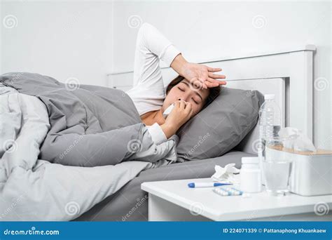 asian woman feeling sick and sleeping in blanket on the bed while using tissue to cough