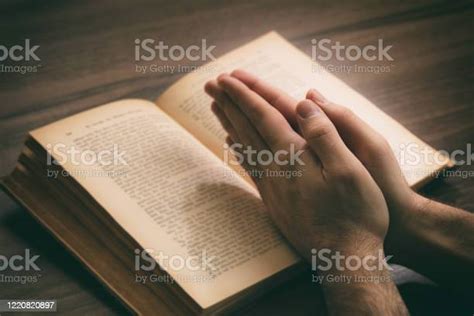 Hands Clasped In Prayer Over A Holy Bible Wooden Table Background Stock