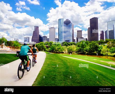Riding Bikes On Paved Trail In Houston Park View Of River And Skyline Of Downtown Houston