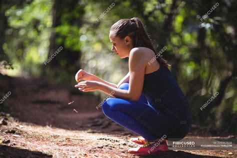 Woman In Squatting Position In Forest Walkway On A Sunny Day Holding