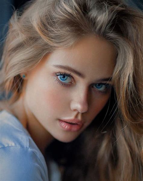A Close Up Of A Woman With Blue Eyes And Blonde Hair Wearing A Light