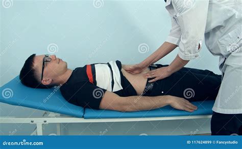 Female Doctor Examining The Abdomen Of Male Patient Lying On The