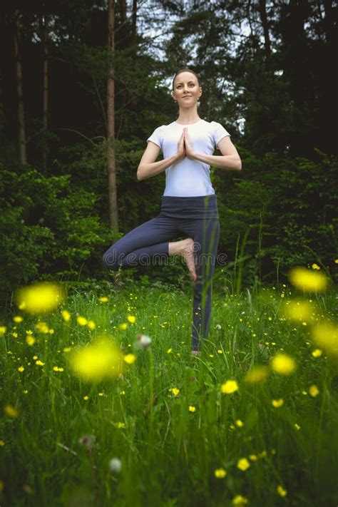 Happy Young Woman Standing In Yoga Pose Vrikshasana On The Grass Stock