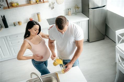 Pregnant Wife In Kitchen With Husband Pouring Orange Juice Stock Image Image Of Inside