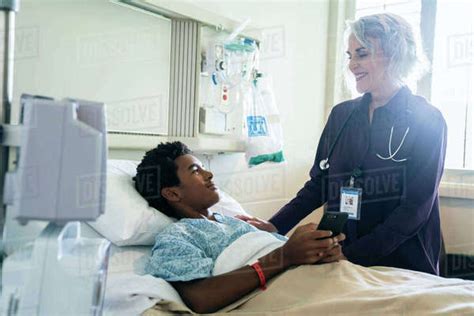 Doctor Comforting Boy In Hospital Bed Holding Cell Phone Stock Photo