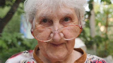 Old Woman In Eyeglasses Looking Into Camera And Smiling Outdoor
