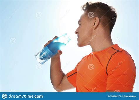 Young Sporty Man Drinking Water From Bottle Against Blue