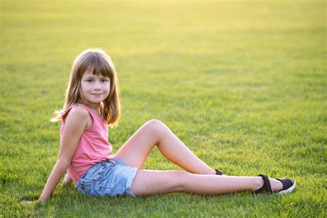 Young Happy Child Girl Resting While Sitting On Green Grass Lawn On