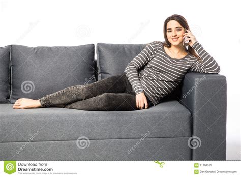 Happy Young Woman Talking Cell Phone While Lying On Sofa On White Stock