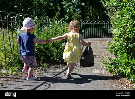 Two Young Children Holding Hands And Walking Away Down A Footpath In