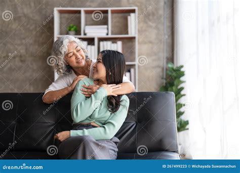 Loving Adult Daughter Hugging Older Mother Standing Behind Couch At