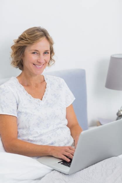 premium photo smiling blonde woman sitting in bed using laptop