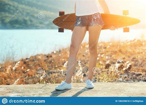 Beautiful Young Girl In Short Shorts Stands With Longboard In Sunny