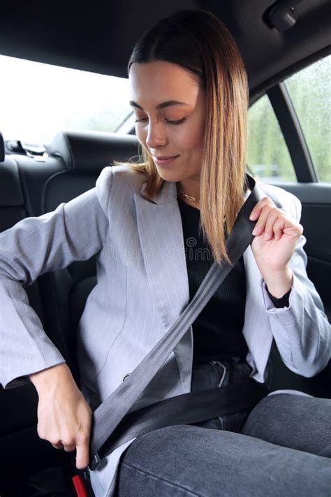 Businesswoman Sitting In Back Seat Of Taxi Or Car Putting On Safety