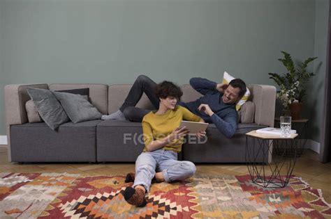 Couple Relaxing Together In The Living Room And Sharing Digital Tablet
