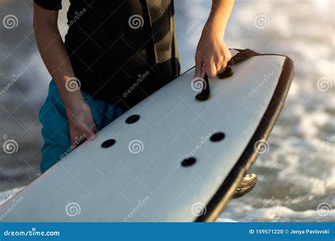 Close Up Detail Of Little Boy Holding Surfboard On Beach At Waters Edge