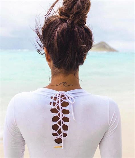 A Woman Standing On The Beach With Her Back Turned To The Camera Wearing A White Top