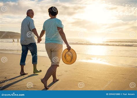 off into the sunset they go a mature couple holding hands while walking on the beach stock