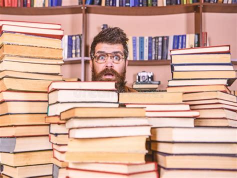 Man Nerd On Surprised Face Between Piles Of Books In Library